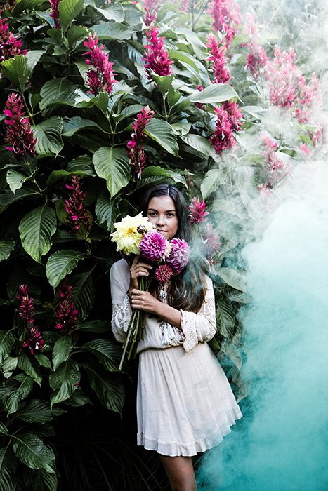 Девушка стоит и держит цветы, с правой стороны к ней приближается большая струя дыма