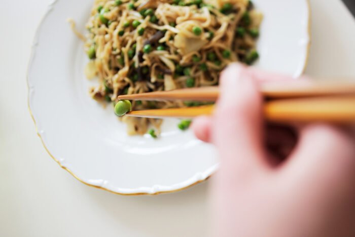 Фотография тарелки с лапшой и руки, держащей палочки для еды