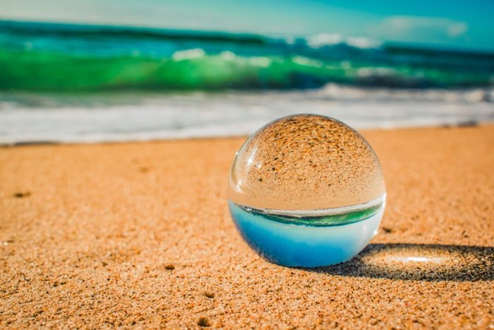 Фотография хрустального шара на пляже, отражающего море и песок