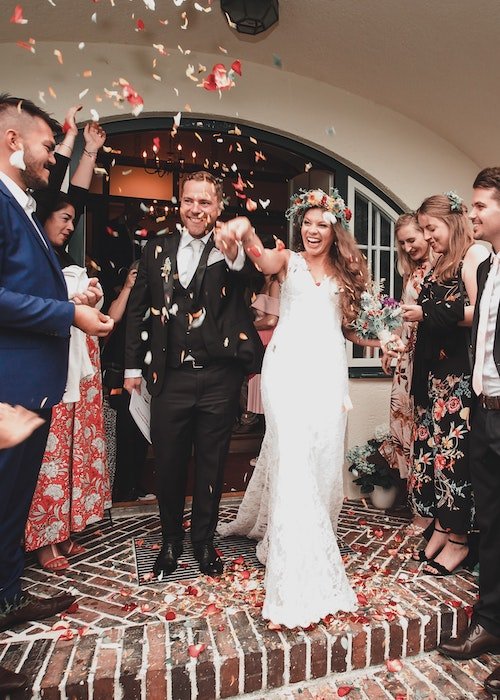 Снимок жениха и невесты, покидающих церемонию, с конфетти в воздухе