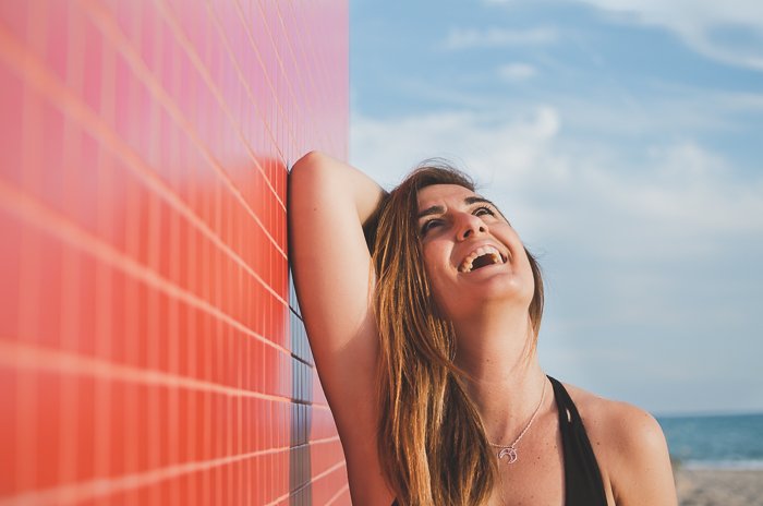 Женщина смеется в лучах солнца рядом с красной стеной