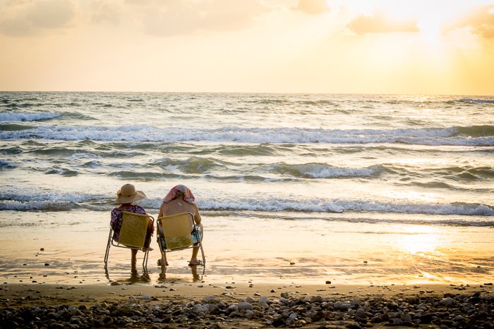 Пожилая пара сидит у самого моря в желтых походных креслах