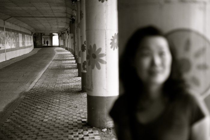 размытый черно-белый портрет девушки, стоящей на фоне каменной колонны