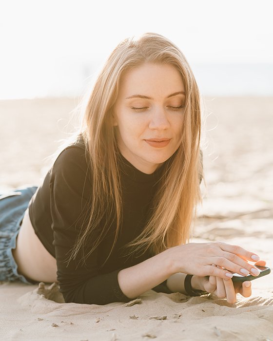 Молодая красивая женщина с длинными волосами отдыхает на песчаном пляже в контровом свете.