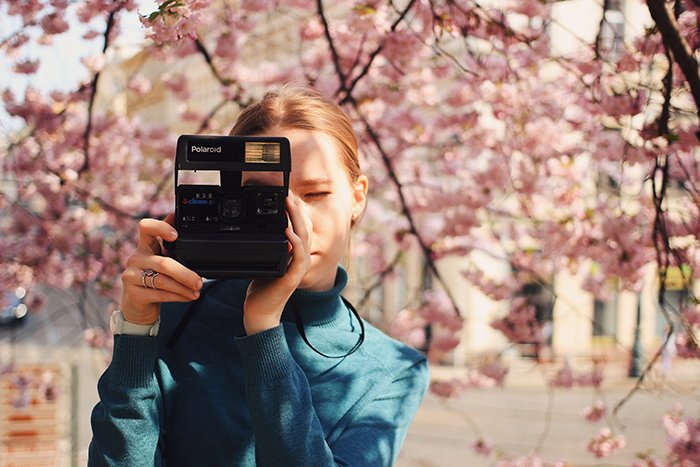 девушка фотографируется с камерой Polaroid под цветущей сакурой