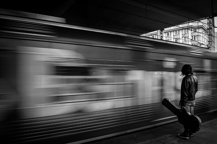 человек с гитарным чехлом стоит у движущегося поезда