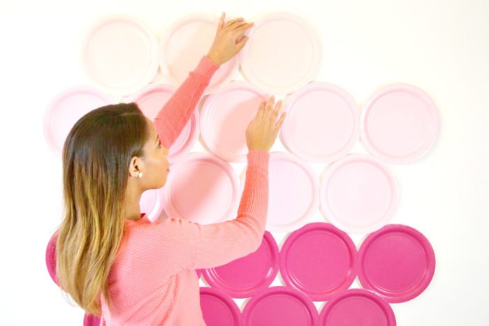 Женщина ставит розовые бумажные тарелки на стену