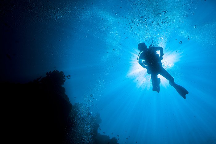 Дайвер сфотографирован под водой в композиции негативного пространства.