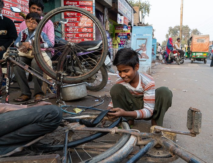 мальчик меняет велосипедную шину на улице в Агре, Индия.
