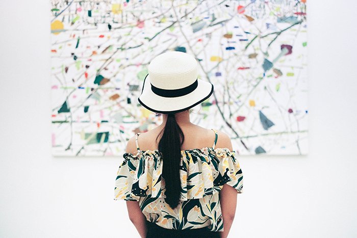 Девушка в бело-черной шляпе смотрит на абстрактную картину