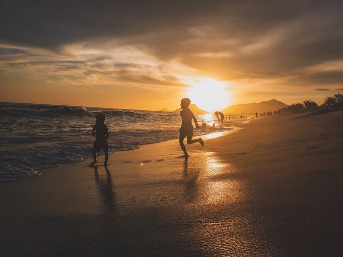 Два маленьких мальчика бегут по пляжу при слабом освещении