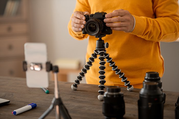 Руки профессионального стокового фотографа фиксируют фотокамеру на штативе на столе.