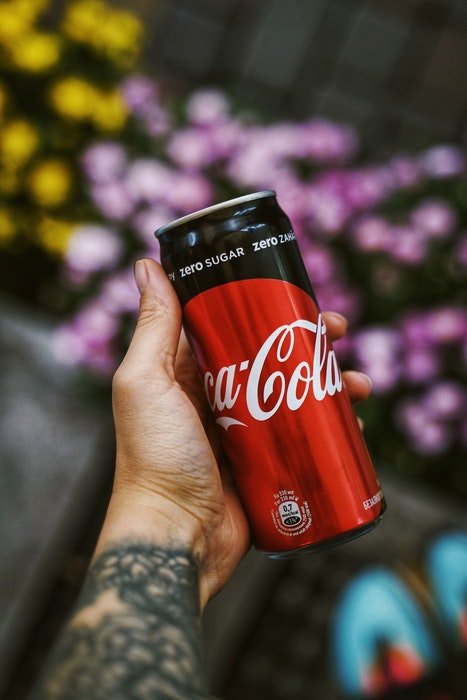 Фотография рекламы продуктов питания, на которой рука держит кока-колу на цветочном фоне