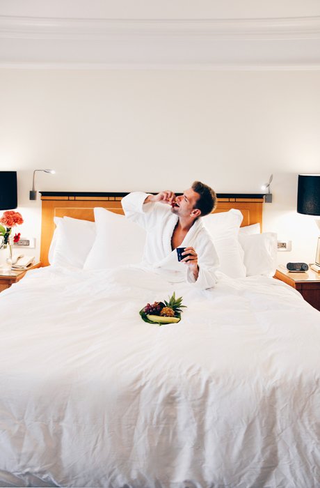 Мужчина на кровати в отеле ест из миски свежие фрукты