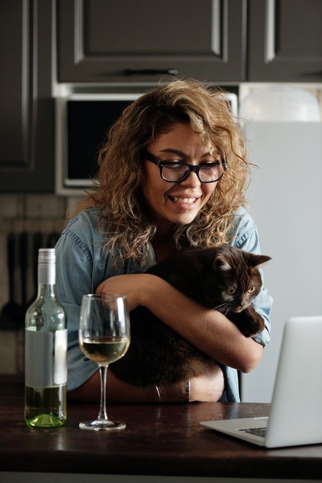Милый портрет кудрявой девушки, держащей кошку перед ноутбуком