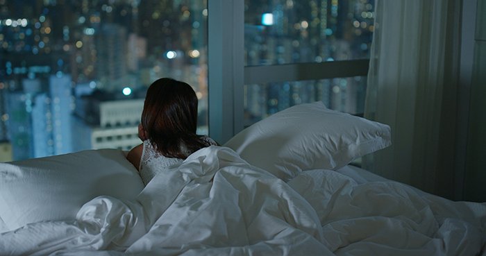 Женщина смотрит на город из окна ночью.