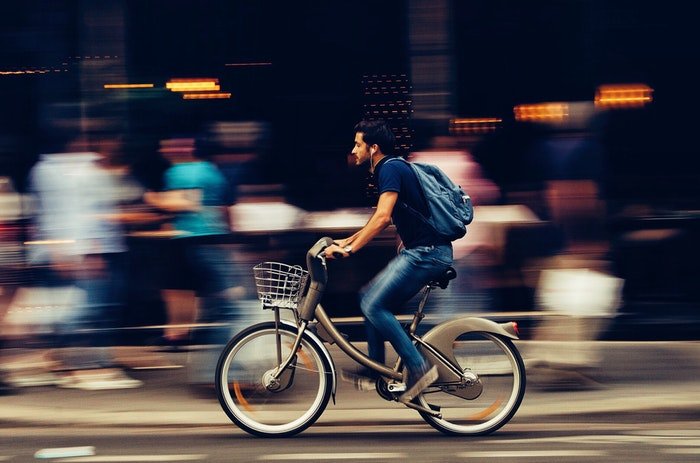 Мужчина едет на велосипеде мимо оживленного рынка