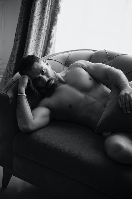 Черно-белое будуарное фото мужчины-модели, лежащего на диване