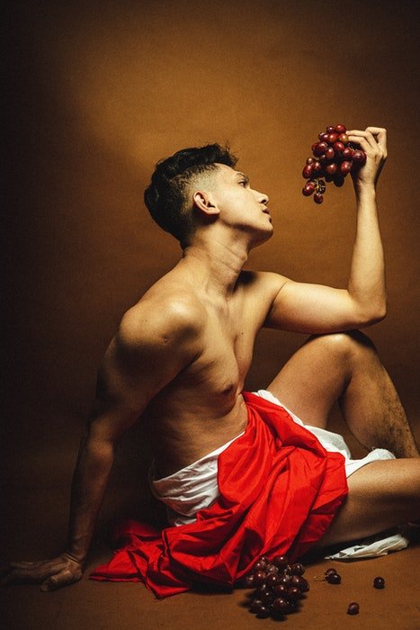 Фотография мужской модели в древнегреческом стиле в позе с виноградом