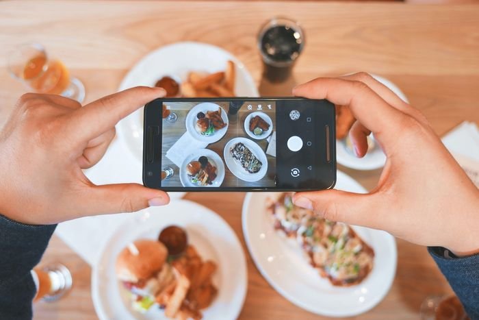 фото рук, держащих смартфон для фотографирования тарелок с едой