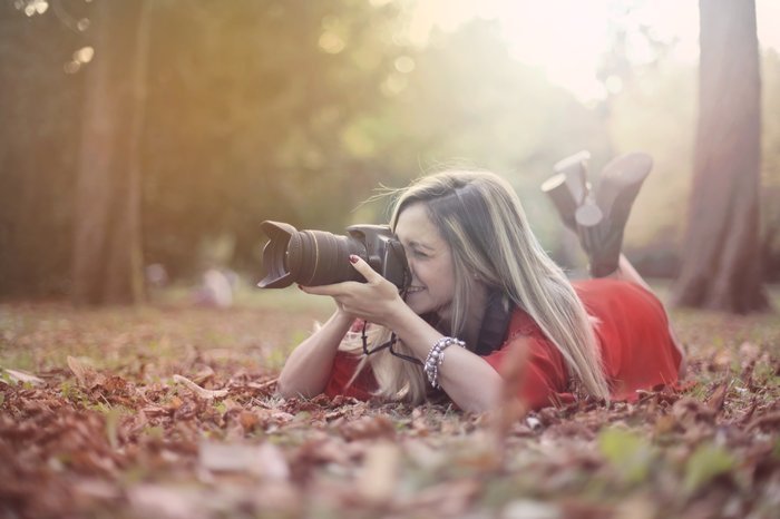 Девушка лежит в осенних листьях, чтобы сделать фото с зеркальным фотоаппаратом