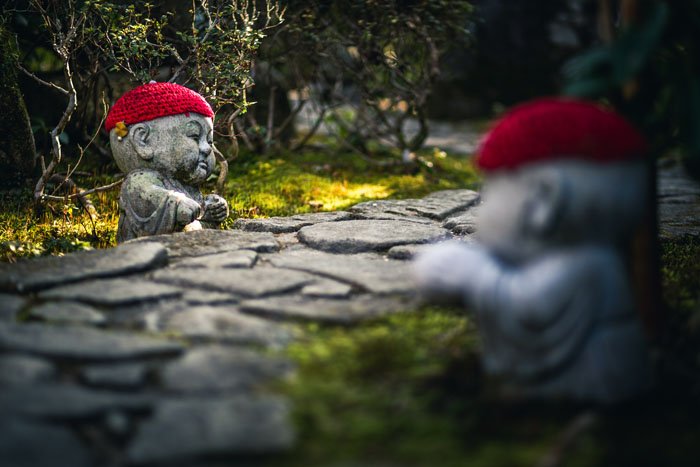 Две каменные скульптуры Будды в красных вязаных шапочках