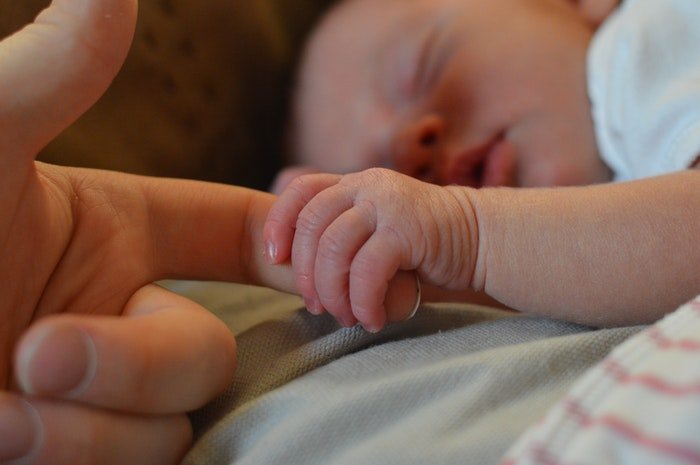Новорожденный ребенок держит палец матери