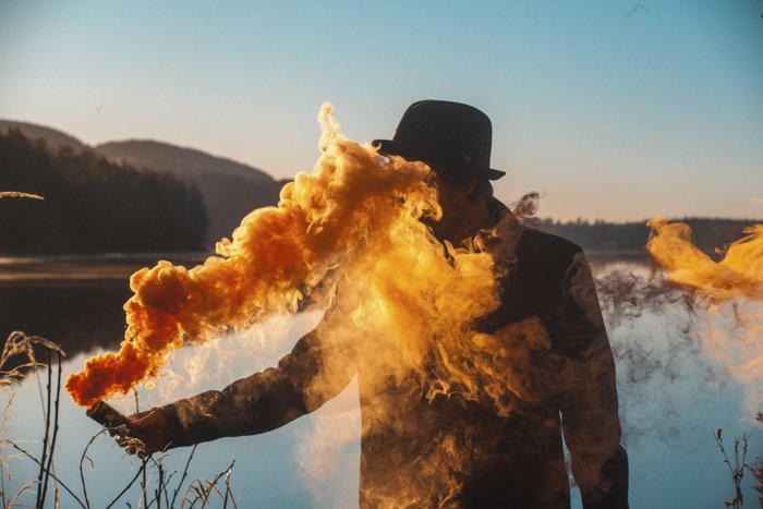 Человек, держащий дымовую гранату, выпускающую ярко-желтый дым на фоне пейзажа