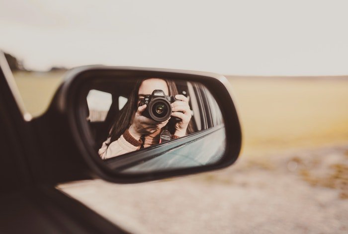 Девушка делает автопортрет в боковое зеркало автомобиля