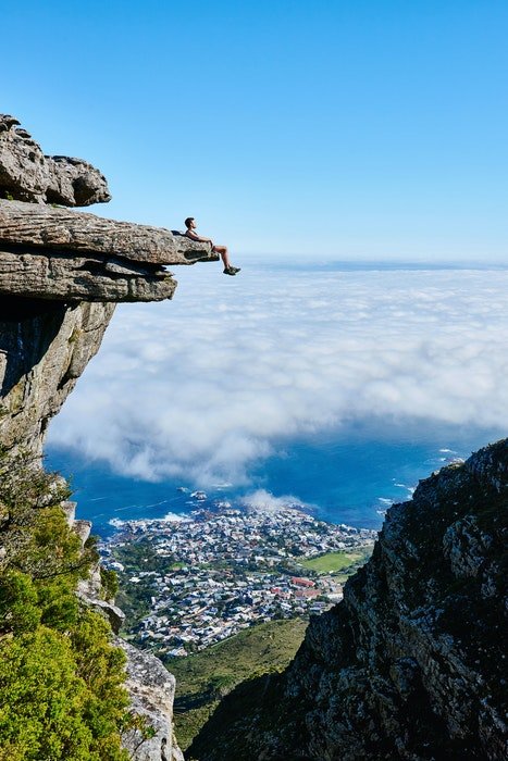 изображение альпиниста, отдыхающего на скале с городом на дальнем фоне