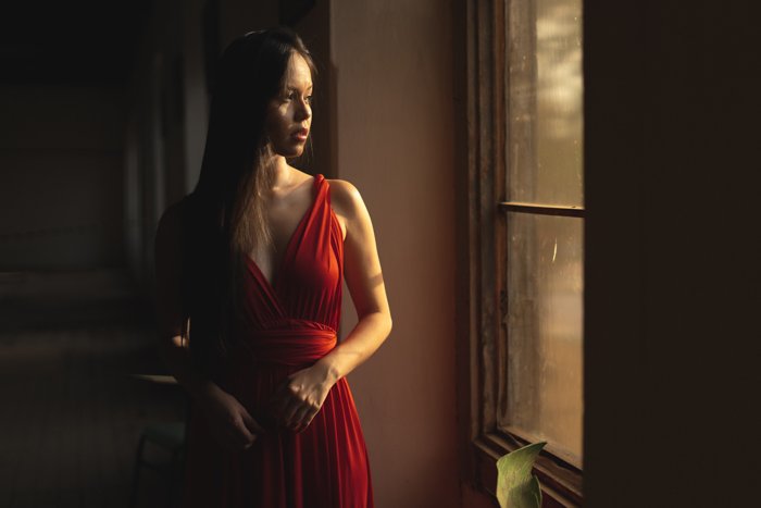 фото женщины в красном платье, стоящей возле окна и смотрящей на улицу