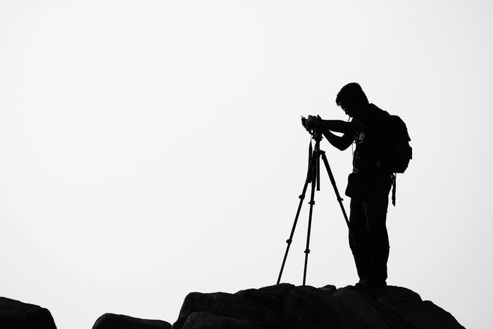 Силуэт фотографа, устанавливающего камеру на штатив