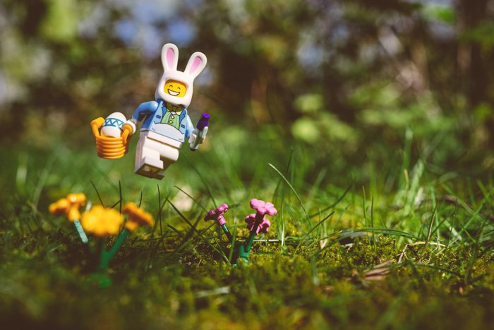Милая игрушечная фотография фигурки лего, одетая как пасхальный кролик, скачущая по траве
