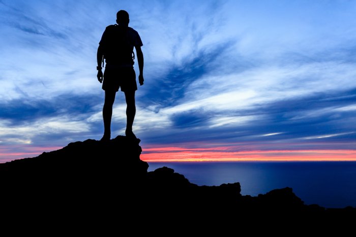 Силуэт человека в походе в горах, закат и океан над красивым голубым небом. Male hiker walking on top of mountain looking at beauty night landscape.