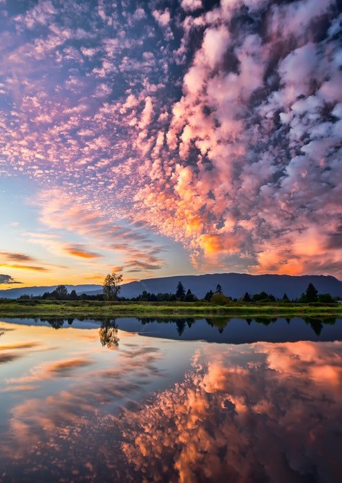фотография облаков вверху, отраженных в озере внизу с розовыми оттенками