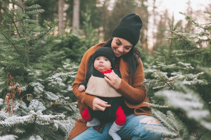 Сладкая рождественская фотография женщины, держащей ребенка на руках перед елкой на открытом воздухе