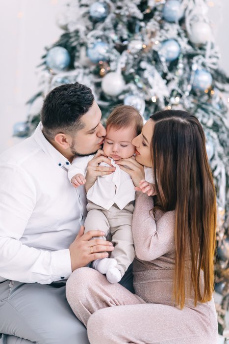 Sweet first Christmas photo of the couple holding their baby in front of christmas tree
