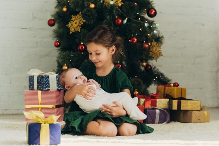 Маленькая девочка держит новорожденного ребенка для их первой рождественской фотосессии