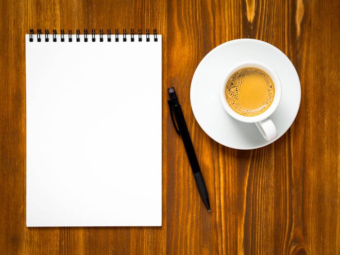 Блокнот с чистой страницей для записи списка дел, чашка кофе и ручка на деревянном коричневом столе