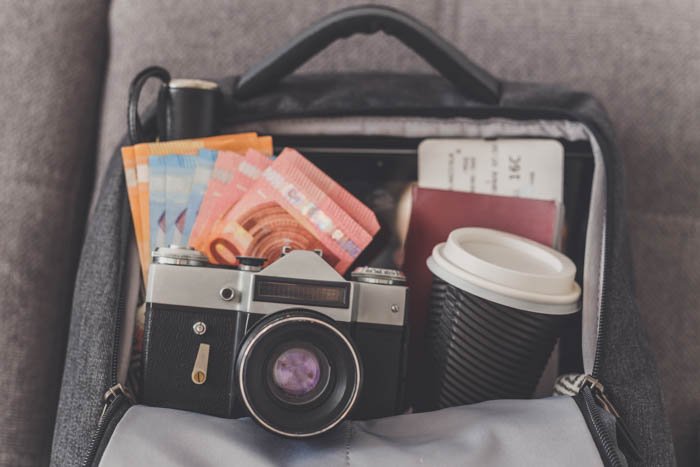 Открытый рюкзак с вещами, необходимыми для фотографии в путешествии, такими как камера, деньги, паспорт и билеты