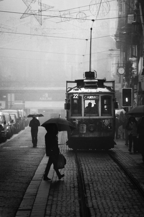 черно-белое изображение мужчины с зонтом, переходящего дорогу в трамвае