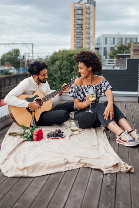 Изображение романтической пары на пикнике, пока парень играет на гитаре