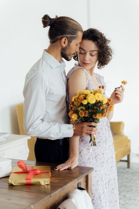 Интимное изображение молодой пары, когда парень держит ведро с цветами над девушкой со спины.