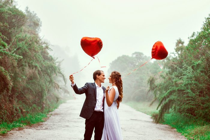 Фотография элегантной пары, держащей воздушные шары в форме сердца.