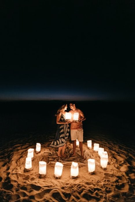 счастливая пара стоит на пляже, окруженная фонарями