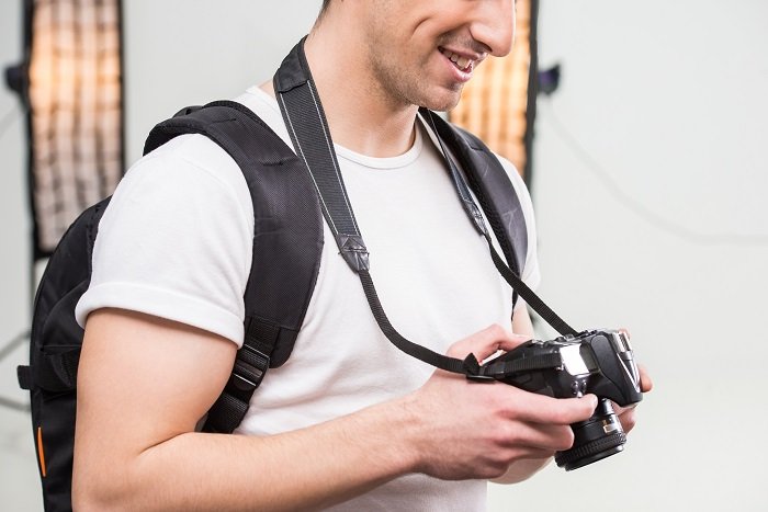 Молодой фотограф с камерой в профессионально оборудованной студии настраивает высокоскоростную синхронизированную вспышку на своей зеркальной камере