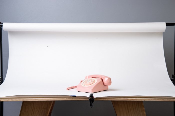 Белая бесшовная бумага, покрывающая стол с розовым телефоном на нем