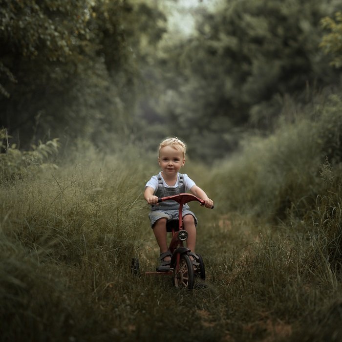 ребенок едет на трехколесном велосипеде по лесной тропе