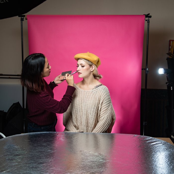 Женщина наносит макияж на модель в маленькой студии