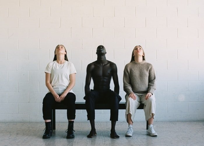 Редакционное изображение трех людей, сидящих на скамейке и смотрящих вверх, с белой цементной стеной за ними